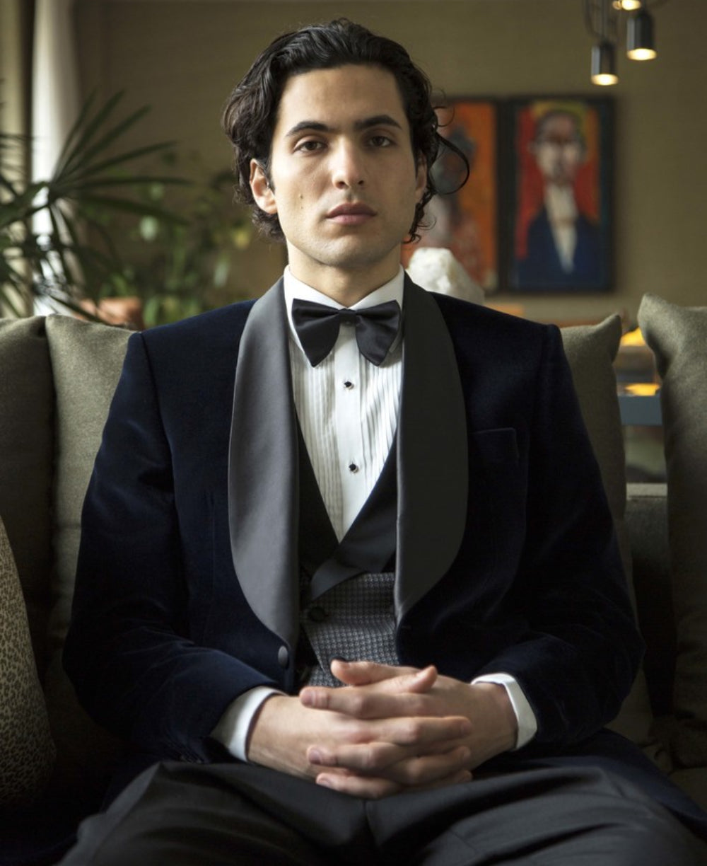 Man wears black dinner jacket with silk-trimmed lapels, a black and white waist coat and white shirt, bow tie and black trousers.