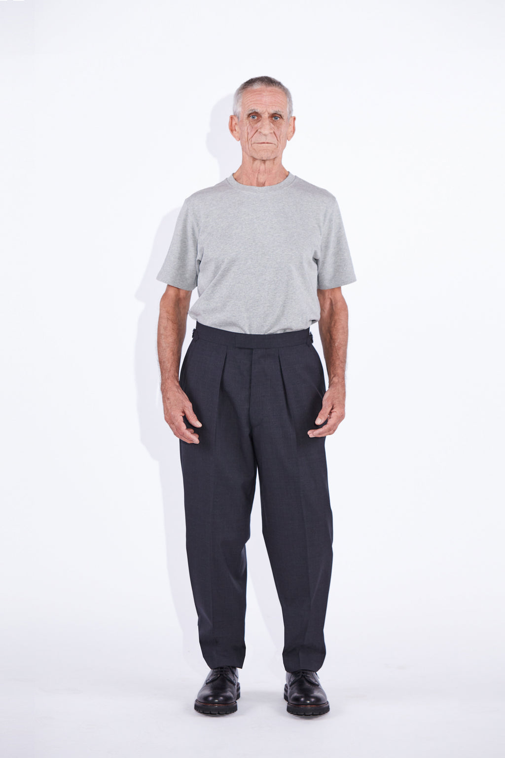 Model wears Casely-Hayford Ezra Anthracite Fresco Relaxed Tapered Leg Wool trousers.
