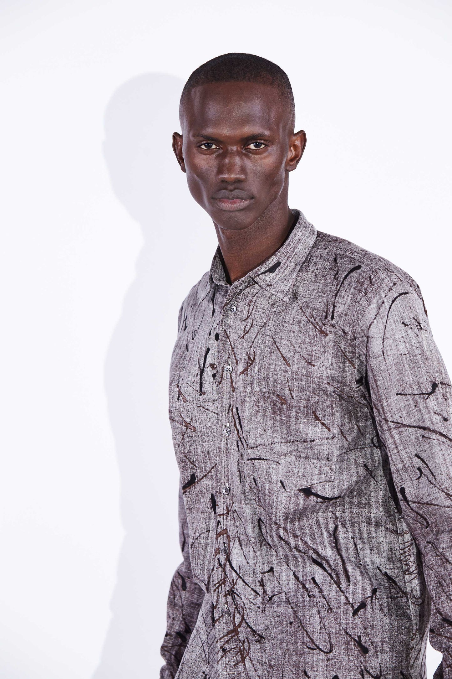 A man stands in a brown pattern shirt looks to camera