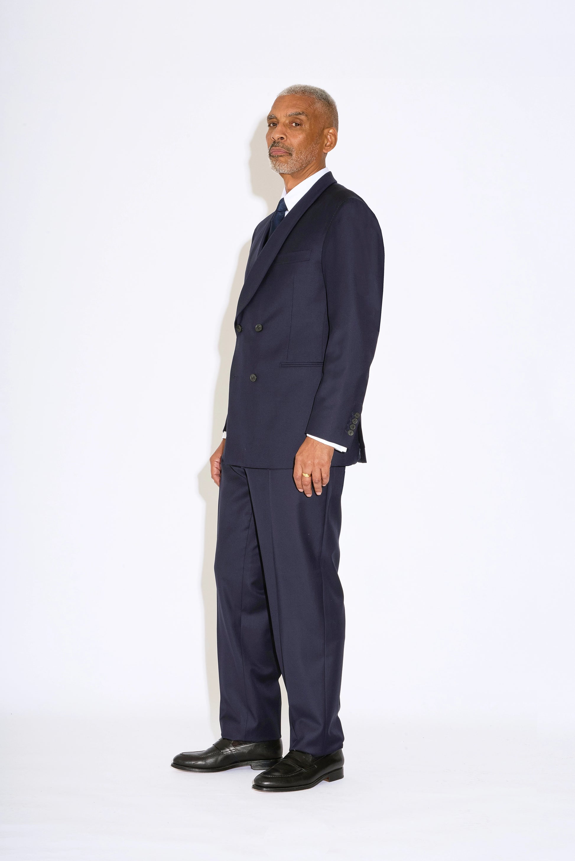 Casely Hayford Hendrix double breasted suit: Model is wearing a navy fitted relaxed shoulder line and soft shawl lapels blazer with matching straight leg trousers. Side view