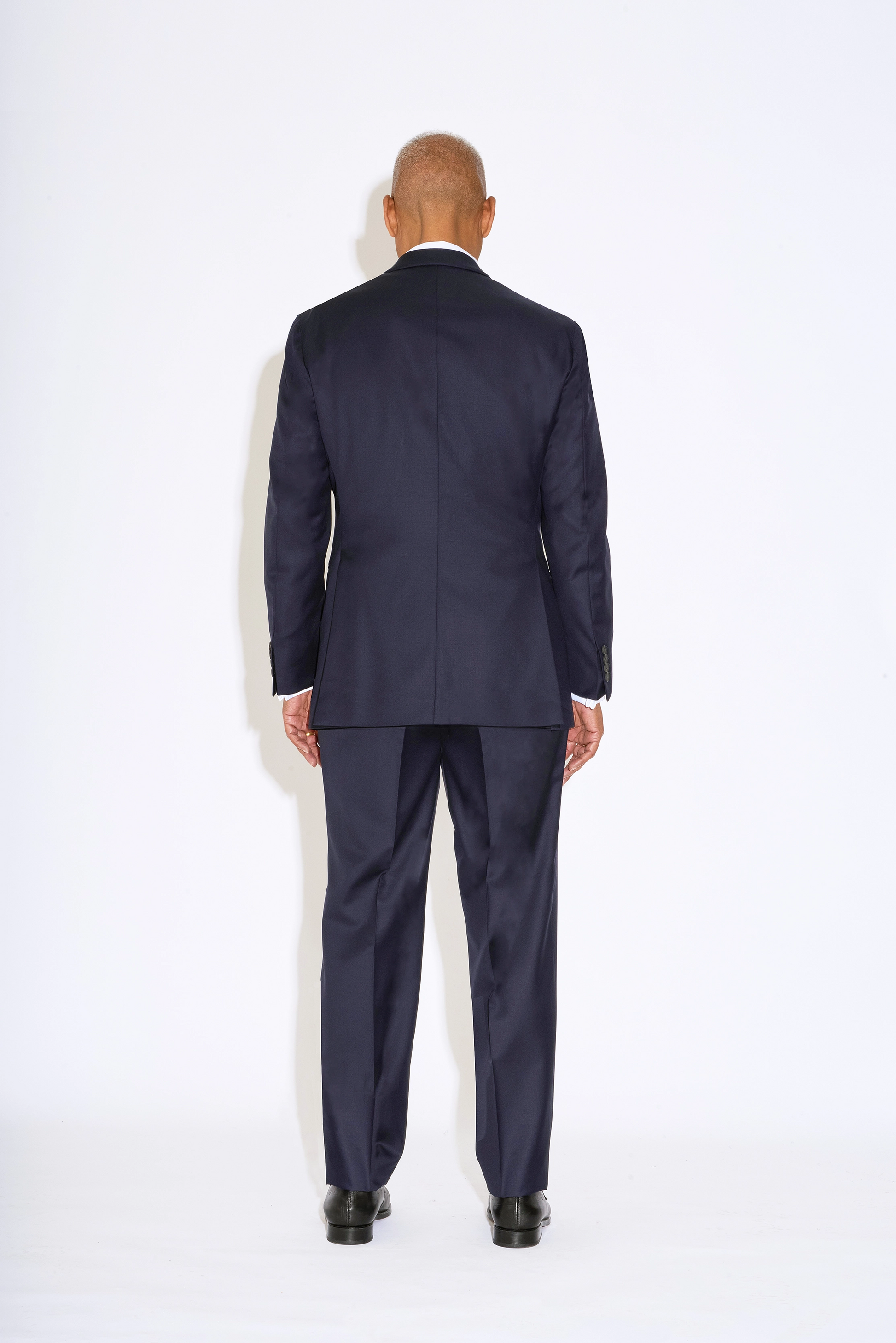 Casely Hayford Hendrix double breasted suit: Model is wearing a navy fitted relaxed shoulder line and soft shawl lapels blazer with matching straight leg trousers. Back view