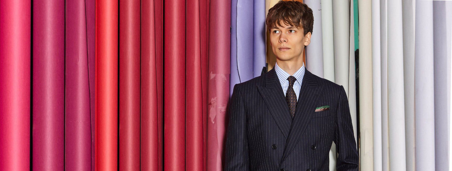 Man wears pinstripe double breasted navy blazer with blue and white striped shirt and navy, read and white dot tie.