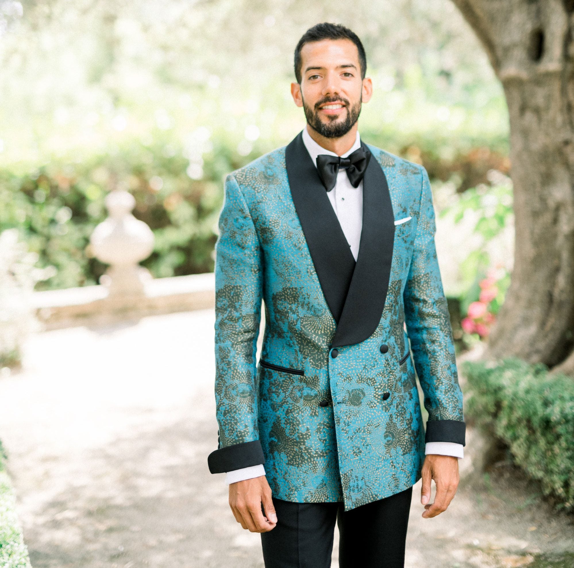 Man wears teal curved black lapel dinner jacket with black cuffs, white shirt and black bowtie. Black trousers