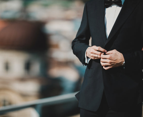 man buttons his black single button shirt with black trousers, white shirt and black bow tie